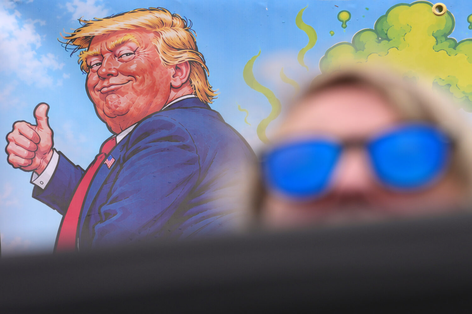 A protester wears sunglasses and sits in front of a poster depicting U.S. President Donald Trump du...
