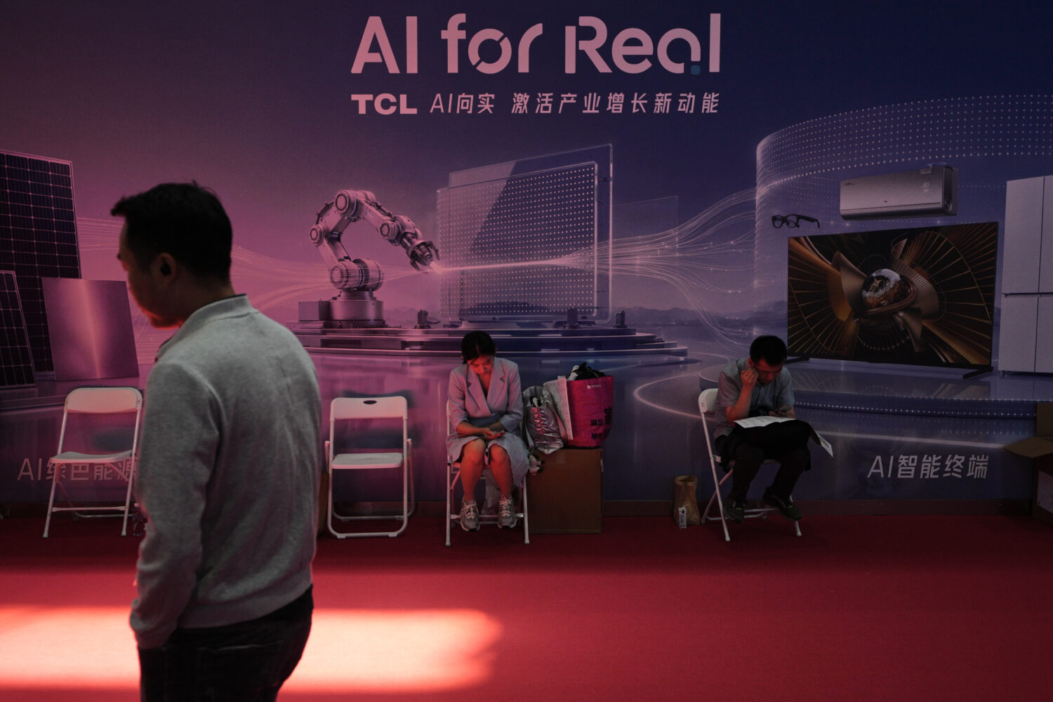 A man walks by as workers rest near a board promoting Artificial Intelligence (AI) at the China Int...