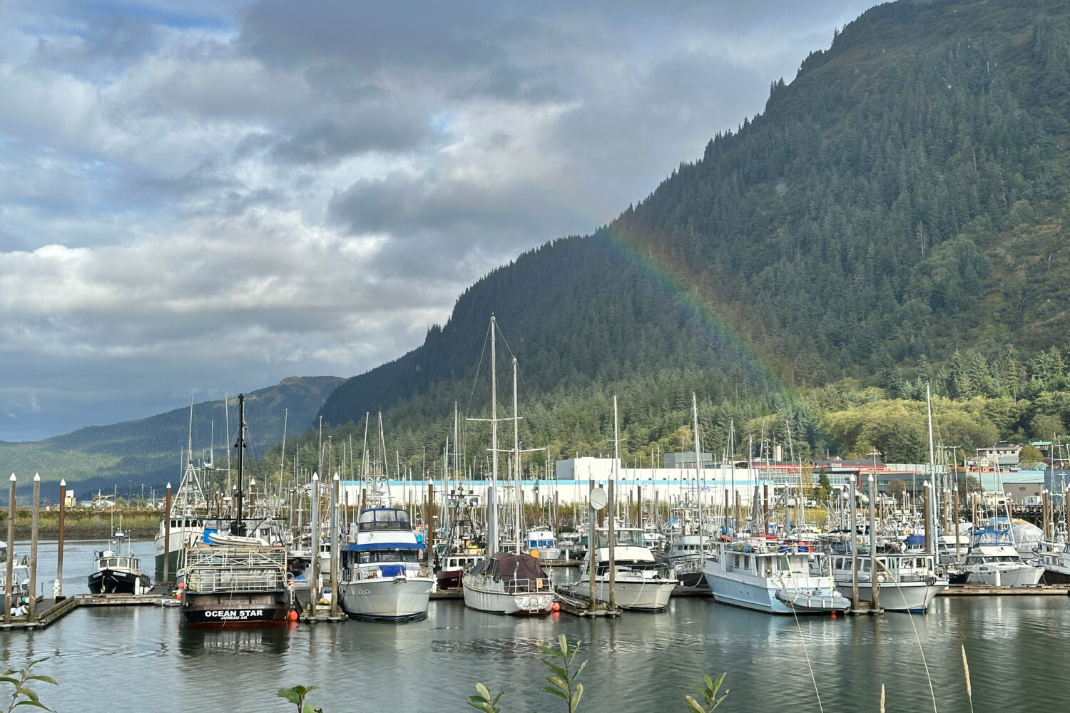 This photo taken with a smartphone shows a partial rainbow arching over boats docked in a harbor in...