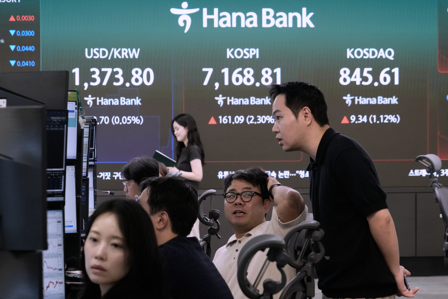 Currency traders work near a screen showing the Korea Composite Stock Price Index (KOSPI) and the f...