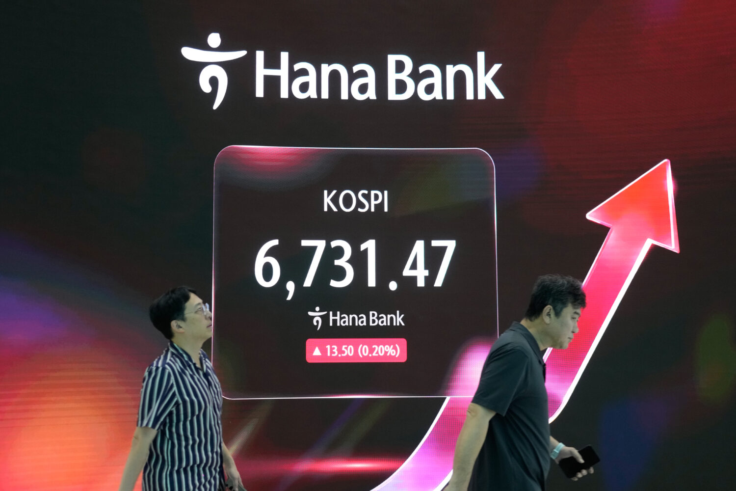 Currency traders pass by a screen showing the Korea Composite Stock Price Index (KOSPI) at the fore...