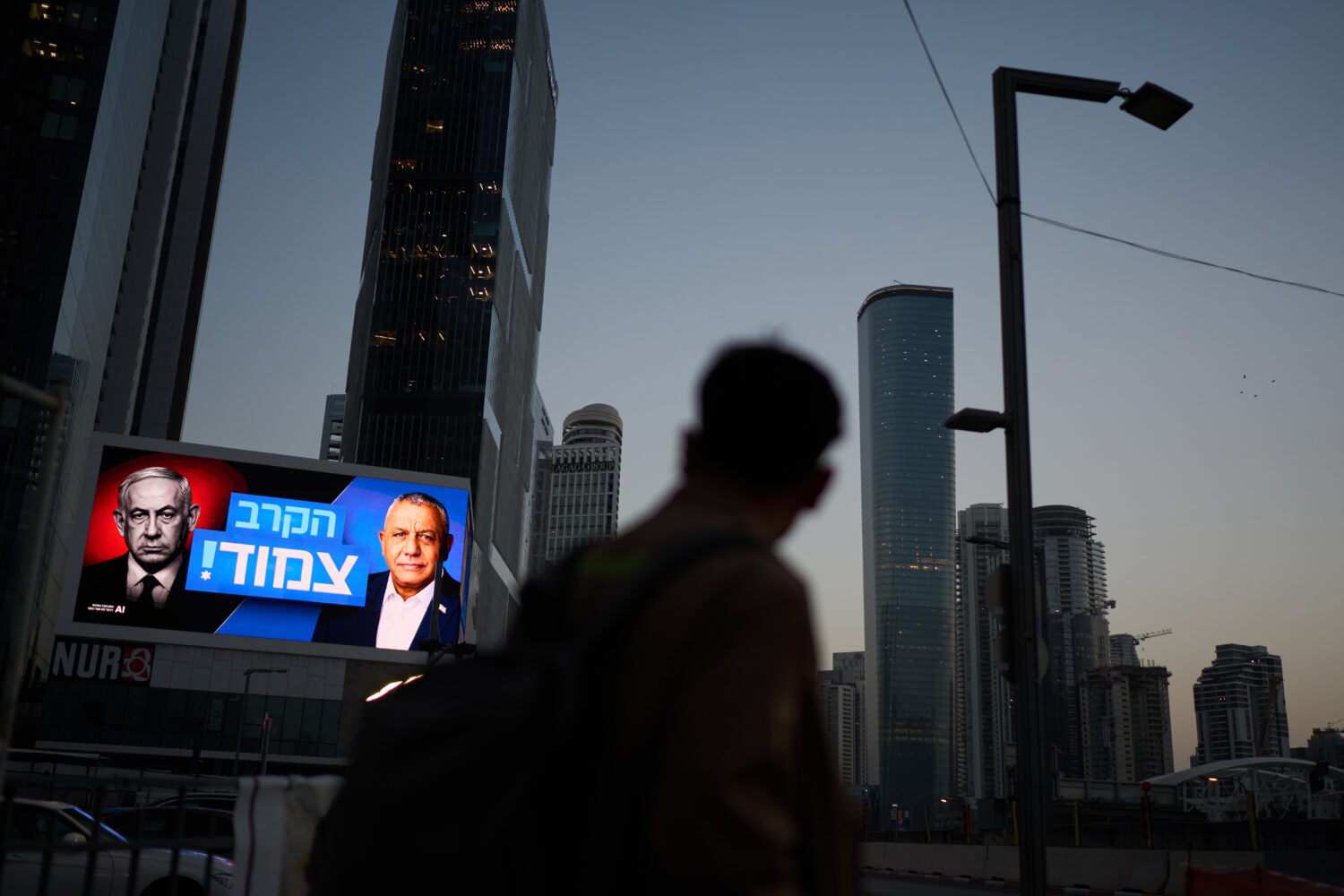 A pedestrian passes a campaign billboard featuring Israeli Prime Minister Benjamin Netanyahu, left,...