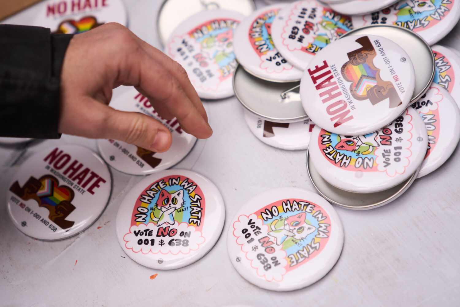 A person picks up a button during a "No Hate in WA State" rally against multiple initiatives on the...