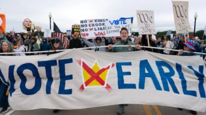 Demonstrators hold up banners as they march across the Memorial Bridge during a No Kings protest in...