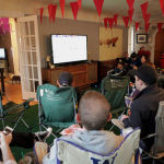 Friends watch the game from lawn chairs, situated on Astroturf, in the living room. 