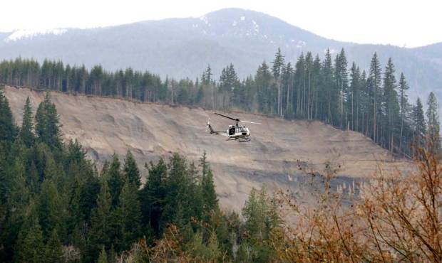A helicopter flies past the area where a deadly mudslide hit on Saturday, Tuesday, March 25, 2014, ...