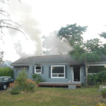 Smoke is seen coming from the roof of a West Seattle house that fire officials say was damaged when a resident used a makeshift blowtorch to try to kill a spider.