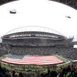In this photo made with a fish-eye lens, military helicopters do a fly-by over CenturyLink Field as a large U.S. flag is displayed during the national anthem before an NFL football game between the Seattle Seahawks and the New York Giants, Sunday, Nov. 9, 2014, in Seattle. The flag and fly by were part of the NFL's Salute to Service tribute to the military. (AP Photo/Scott Eklund)