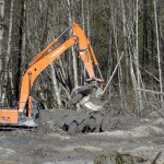 An excavator dislodges and stacks logs buried in deep mud at the scene of a deadly mudslide Wednesday, April 2, 2014, in Oso, Wash. Officials have so far confirmed the deaths of 29 people, although only 22 have been officially identified in information released Wednesday morning by the Snohomish County medical examiner's office. (AP Photo/Elaine Thompson)