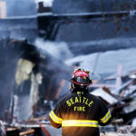 A firefighter looks at the smoldering rubble left from an early morning explosion Wednesday, March 9, 2016, in Seattle. The explosion heavily damaged buildings and injured multiple firefighters. 
