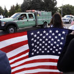 People hold an American flag as they watch a U.S. Forest Service truck in a motorcade pass before a memorial service for three firefighters killed in a wildfire, Sunday, Aug. 30, 2015, in Wenatchee, Wash. Firefighters Richard Wheeler, Andrew Zajac and Thomas Zbyszewski died Aug. 19 in a fire near Twisp, Wash. (AP Photo/Elaine Thompson)