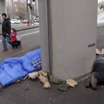 A woman walks a child past people asleep under Interstate 5 near downtown Seattle on Wednesday, Feb. 17, 2016. Even as homelessness declined slightly nationwide in 2015, it increased in urban areas, including Seattle, New York and Los Angeles. (AP Photo/Elaine Thompson)