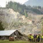 Rescue workers remove one of a number of bodies from the wreckage of homes destroyed by a mudslide near Oso, Wash., Monday, March 24, 2014. The search for survivors of Saturday's deadly mudslide grew Monday to include scores of people who were still unaccounted for as the death toll from the wall of trees, rocks and debris that swept through the rural community rose to at least 14. (AP Photo/seattlepi.com, Joshua Trujillo)