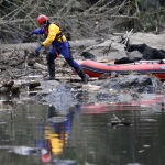 A searcher steps off of his boat to look through debris following a deadly mudslide, Tuesday, March 25, 2014, in Oso, Wash. At least 14 people were killed in the 1-square-mile slide that hit in a rural area about 55 miles northeast of Seattle on Saturday. Several people also were critically injured, and homes were destroyed. (AP Photo/Elaine Thompson)