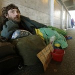 Harold McDuffie II, who says he has been homeless for three years, lies in a sleeping bag on a pedestrian bridge leading to the ferry dock in downtown Seattle on Tuesday, Feb. 9, 2016. Ten years ago, a coalition of leaders came up with a plan to end homelessness by 2015. In that time, the city and county built more than 6,300 housing units and helped nearly 40,000 people find homes. Yet the number of homeless people has continued to climb. (AP Photo/Ted S. Warren)