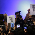 Members of the media scramble with their smart phones and cameras to photograph a picture of the second man, his identity is still not released, who boarded the now missing Malaysia Airlines jet MH370 with a stolen passport, held up by Malaysian police during a press conference, Tuesday, March 11, 2014, in Sepang, Malaysia. One of the two men traveling on the missing Malaysian Airlines jetliner was an Iranian asylum seeker, officials said Tuesday, as baffled authorities expanded their search for the Boeing 777 on the opposite side of the country from where it disappeared days ago with 239 people on board.(AP Photo/Wong Maye-E)